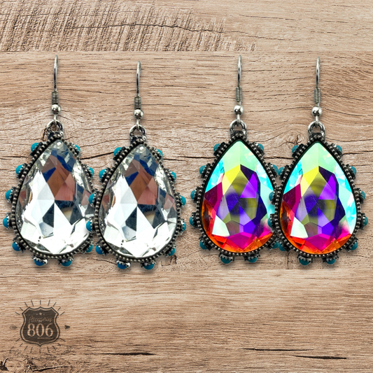 Pair of teardrop-shaped earrings with colorful gemstones on a wooden surface.