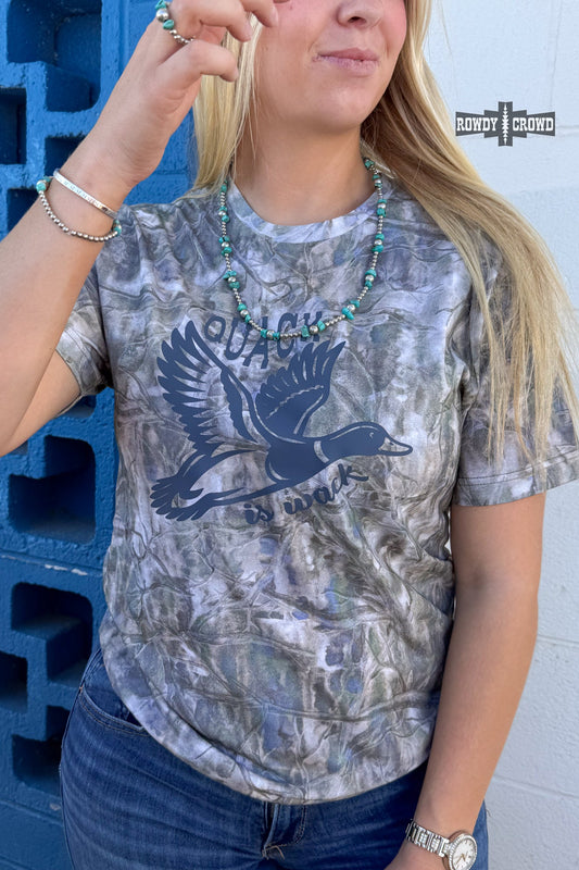 A woman wearing a short-sleeve graphic t-shirt with a gray, white, and blue camouflage pattern and a dark blue flying duck design. The shirt features the text 'QUACK QUACK IN THE MUD'.
